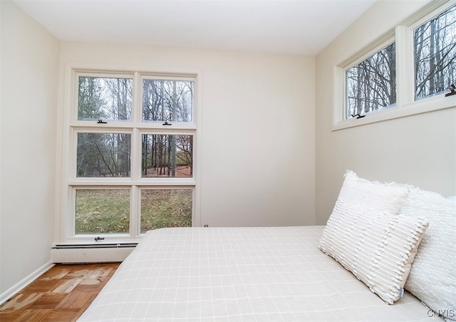 bedroom with multiple windows, light parquet floors, and a baseboard heating unit