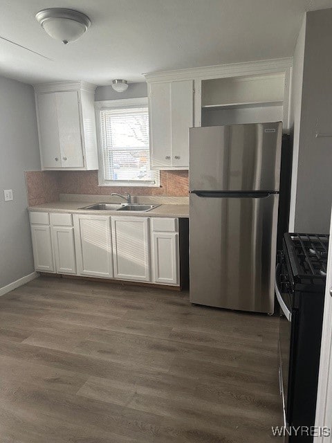 kitchen with stainless steel fridge, black stove, tasteful backsplash, sink, and white cabinets