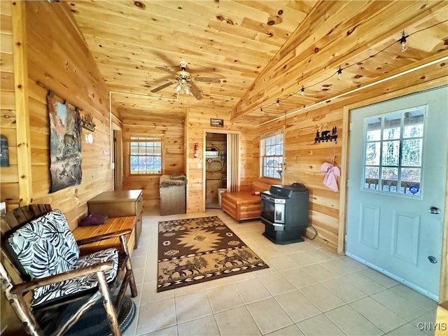 tiled living room with wooden walls, a wood stove, plenty of natural light, and lofted ceiling