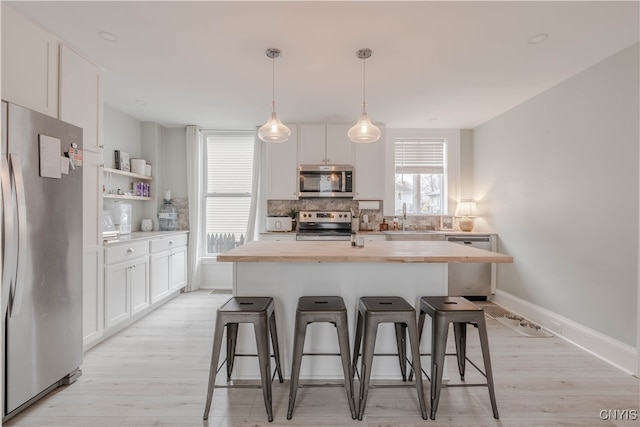 kitchen featuring stainless steel appliances, decorative light fixtures, light hardwood / wood-style flooring, a center island with sink, and white cabinets