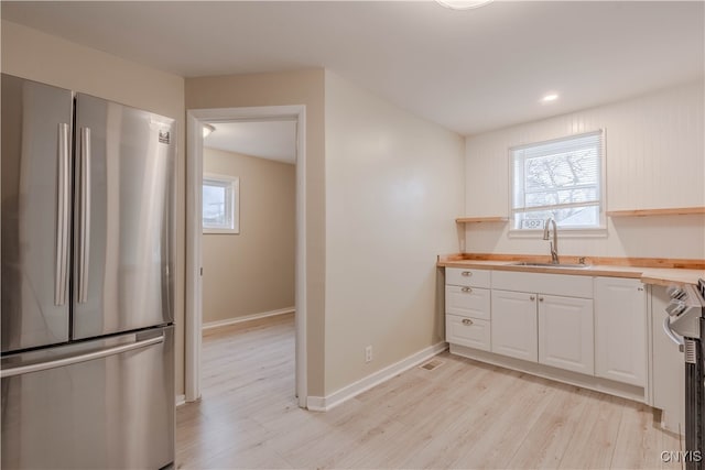 kitchen with sink, stainless steel appliances, butcher block countertops, white cabinets, and light wood-type flooring