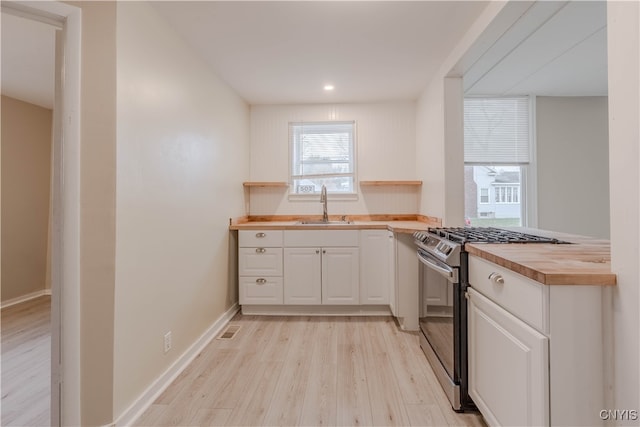 kitchen with sink, light hardwood / wood-style flooring, butcher block countertops, white cabinets, and stainless steel range with gas stovetop