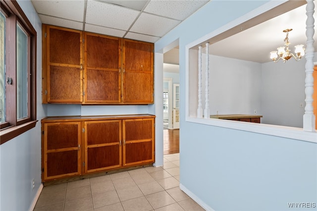 kitchen with pendant lighting, a paneled ceiling, light tile patterned floors, and a notable chandelier