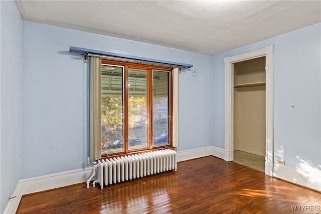 unfurnished bedroom featuring radiator heating unit, dark hardwood / wood-style flooring, a textured ceiling, and a closet