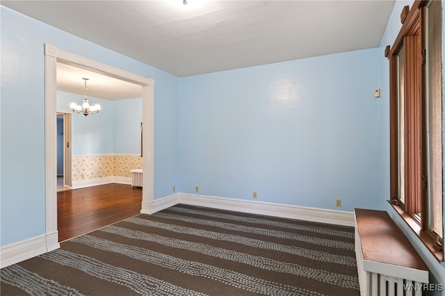 unfurnished room featuring dark hardwood / wood-style flooring, radiator, and an inviting chandelier