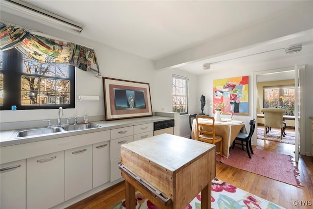 kitchen featuring dishwasher, white cabinets, sink, light hardwood / wood-style flooring, and beam ceiling