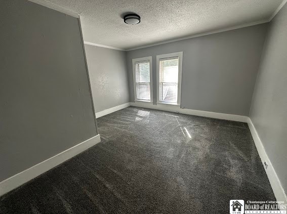 spare room with dark colored carpet, a textured ceiling, and crown molding