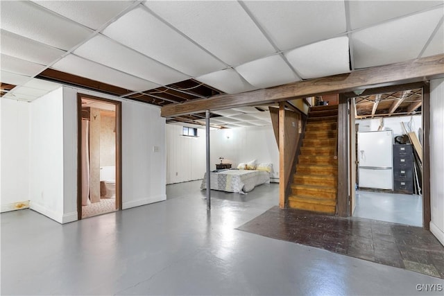 basement with a paneled ceiling and white fridge