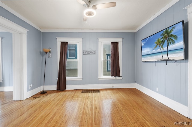 empty room with ceiling fan, light hardwood / wood-style floors, crown molding, and wooden walls