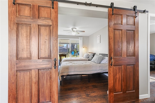 bedroom with a barn door, ceiling fan, and dark wood-type flooring