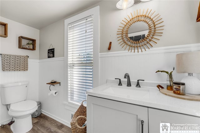 bathroom with a wainscoted wall, toilet, vanity, and wood finished floors