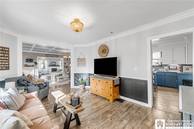 living room featuring ornamental molding, coffered ceiling, light wood-style floors, wainscoting, and a chandelier