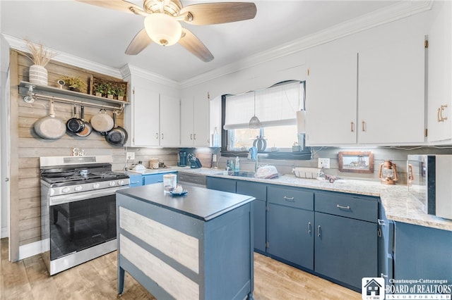 kitchen featuring stainless steel gas range oven, blue cabinets, a sink, crown molding, and white microwave