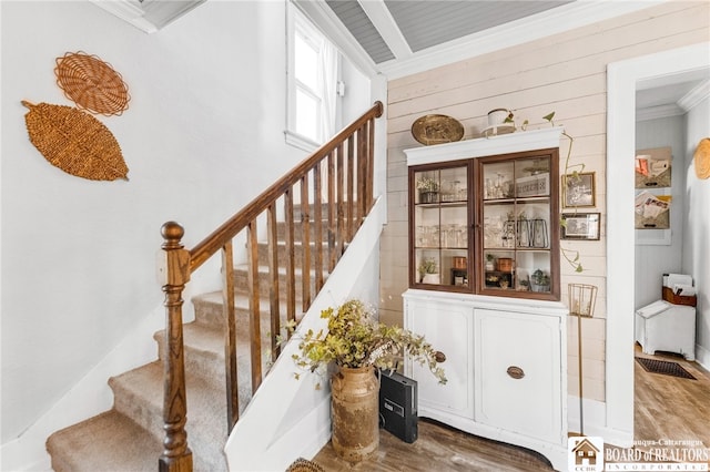 staircase featuring wood walls, wood finished floors, and ornamental molding