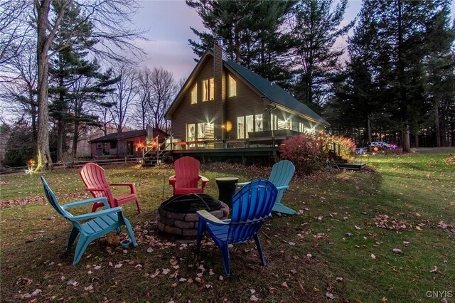 back house at dusk with a yard, an outdoor fire pit, and a wooden deck