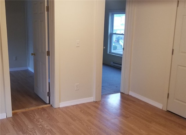 hallway with light wood-type flooring and a baseboard heating unit