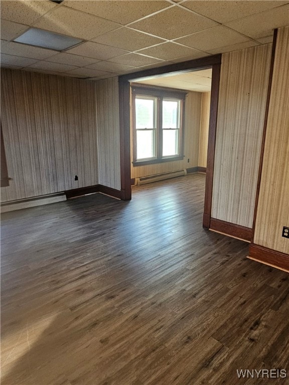 unfurnished room featuring a paneled ceiling, wood walls, dark wood-type flooring, and a baseboard radiator