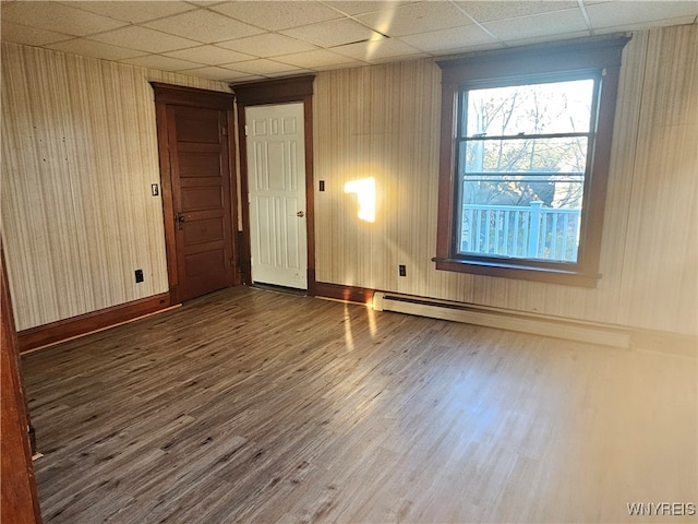 unfurnished room with a paneled ceiling, dark hardwood / wood-style flooring, and a baseboard heating unit