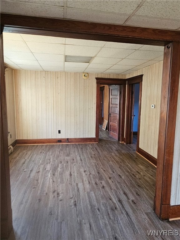 empty room with a paneled ceiling, dark hardwood / wood-style floors, and wooden walls