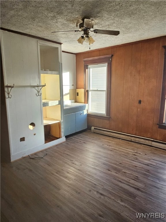 interior space with ceiling fan, a baseboard radiator, dark hardwood / wood-style floors, wood walls, and a textured ceiling