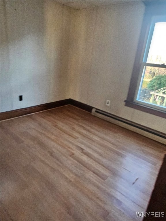 unfurnished room featuring wood-type flooring and a baseboard heating unit