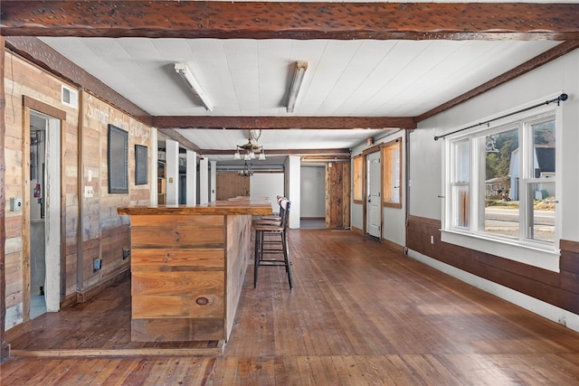 kitchen featuring a breakfast bar, wooden walls, dark hardwood / wood-style floors, beamed ceiling, and a chandelier