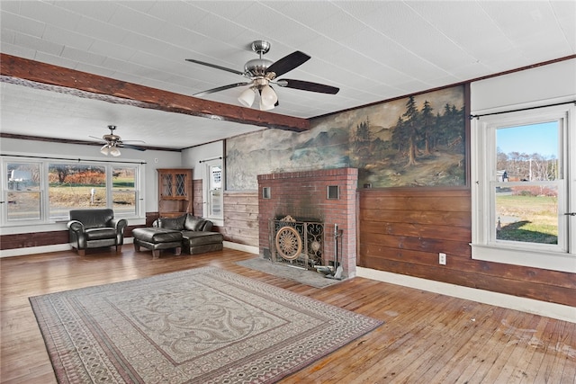 living room with wood-type flooring, a brick fireplace, ceiling fan, and wood walls