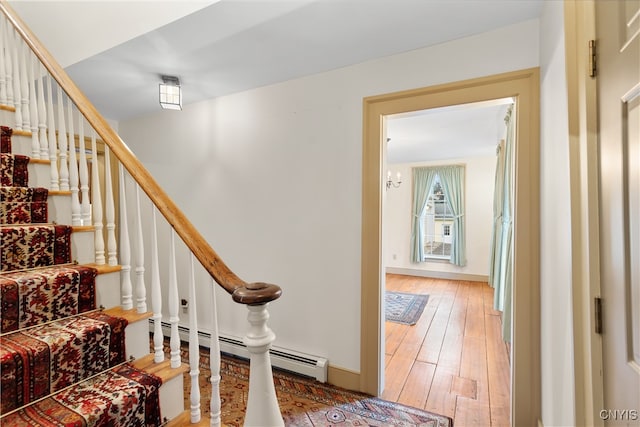 stairway with wood-type flooring, an inviting chandelier, and baseboard heating