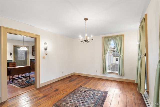 unfurnished room featuring wood-type flooring, baseboard heating, and a chandelier