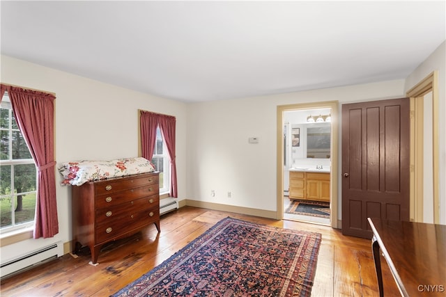 bedroom with a baseboard radiator, light hardwood / wood-style flooring, and ensuite bathroom