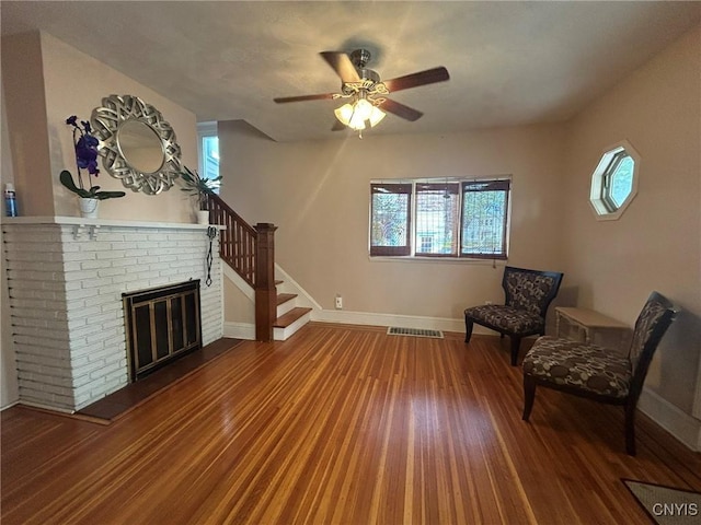 unfurnished room with hardwood / wood-style flooring, ceiling fan, and a brick fireplace