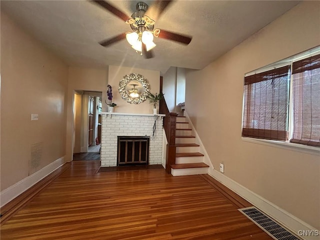 unfurnished living room featuring hardwood / wood-style floors, a textured ceiling, a brick fireplace, and ceiling fan