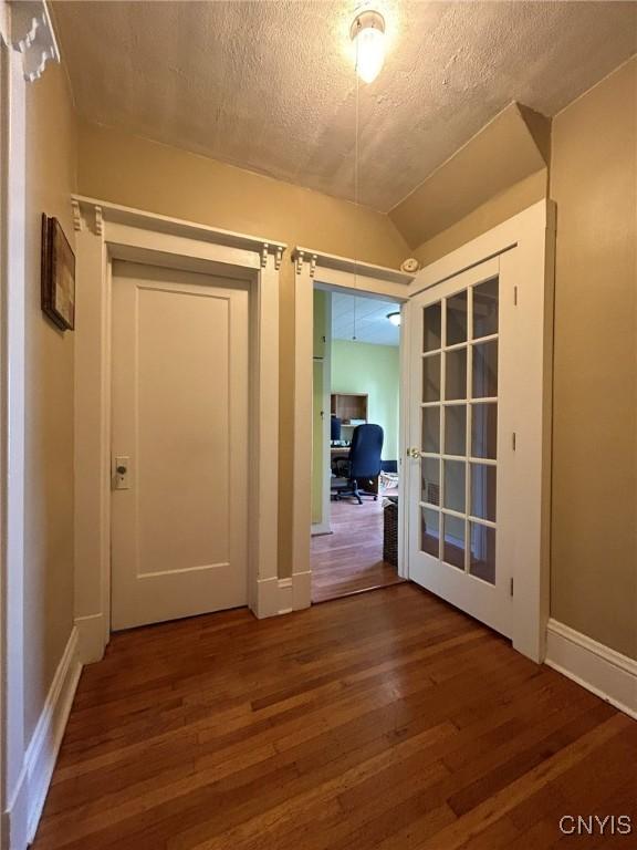 hall with french doors, a textured ceiling, dark hardwood / wood-style floors, and lofted ceiling