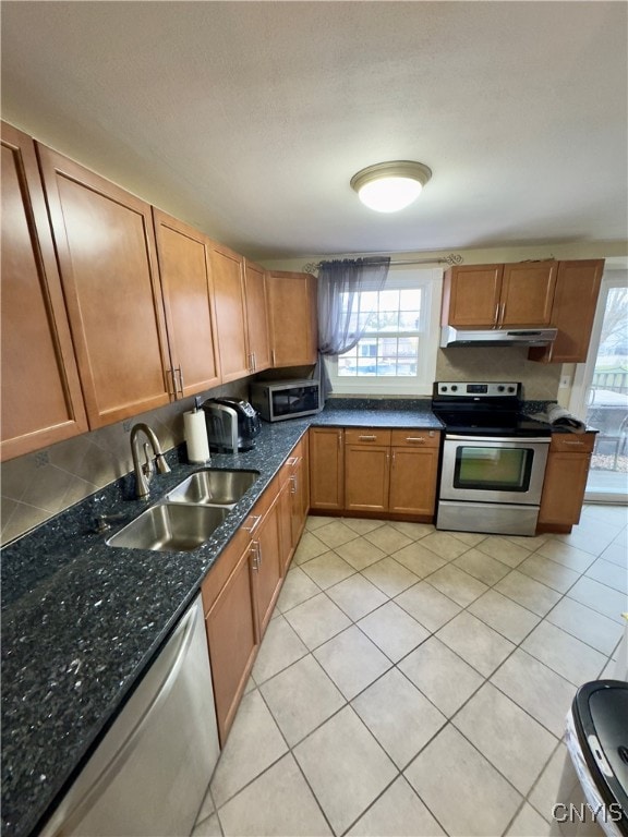 kitchen featuring sink, light tile patterned flooring, dark stone counters, and appliances with stainless steel finishes