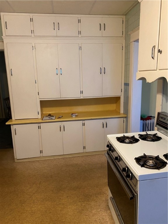 kitchen featuring white gas stove, light colored carpet, and white cabinetry