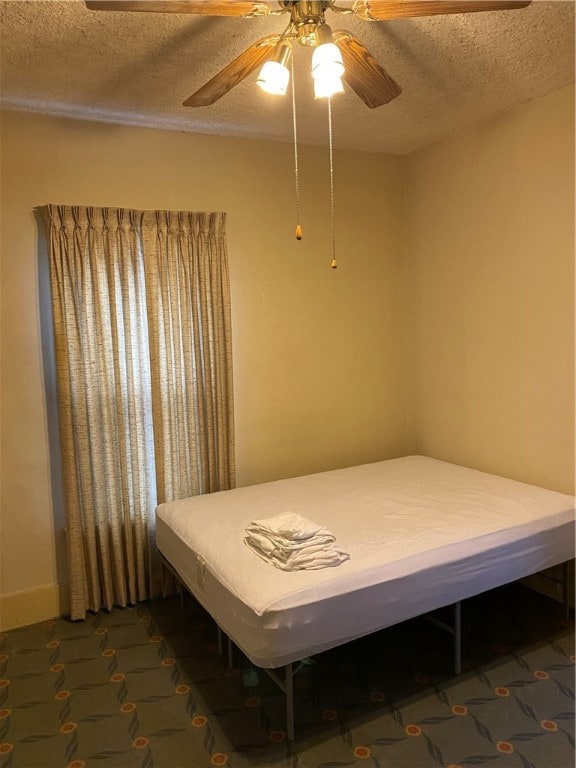 bedroom with dark colored carpet, ceiling fan, and a textured ceiling