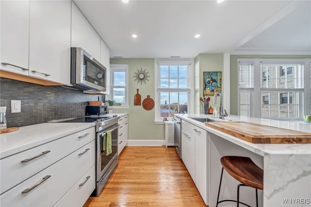 kitchen with appliances with stainless steel finishes, sink, light hardwood / wood-style flooring, white cabinetry, and a breakfast bar area