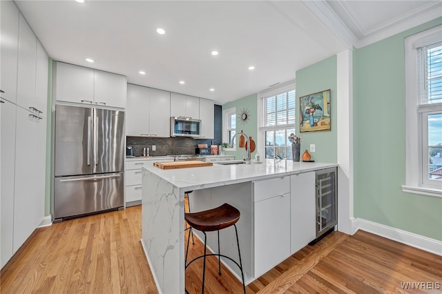 kitchen with white cabinets, ornamental molding, light hardwood / wood-style floors, kitchen peninsula, and stainless steel appliances