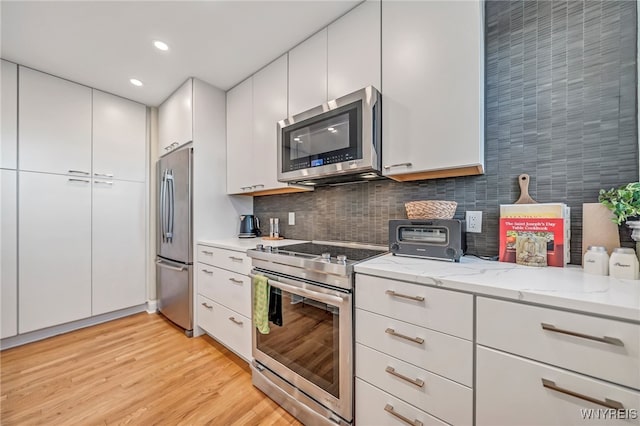 kitchen with white cabinets, decorative backsplash, light stone countertops, light wood-type flooring, and appliances with stainless steel finishes