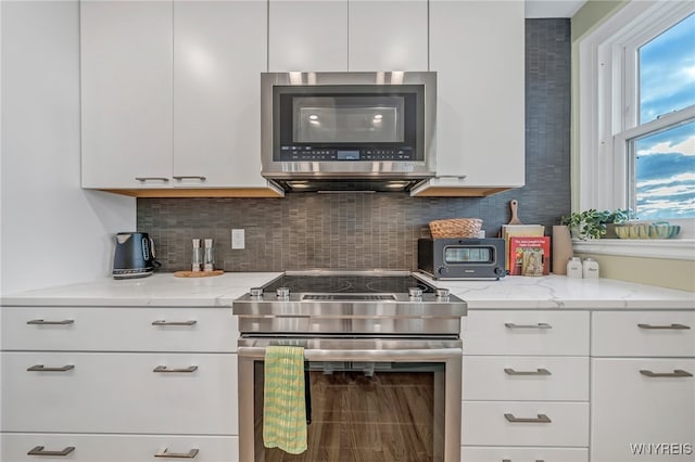 kitchen with decorative backsplash, stainless steel appliances, white cabinetry, and light stone counters