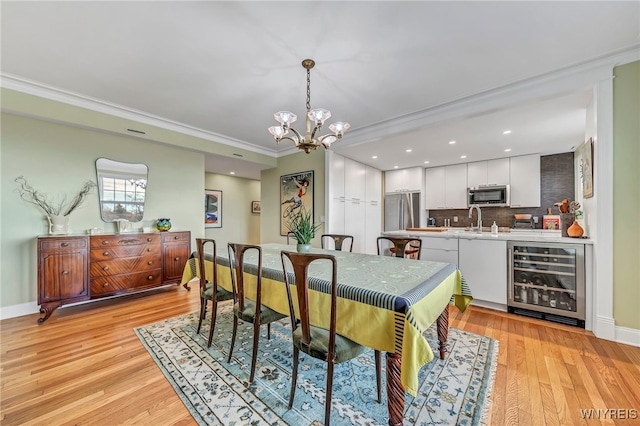 dining space featuring sink, ornamental molding, light hardwood / wood-style floors, beverage cooler, and a chandelier