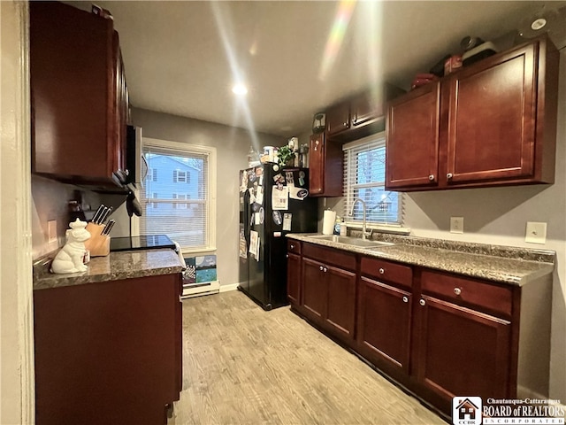 kitchen with black refrigerator, light wood-type flooring, sink, and dark stone counters