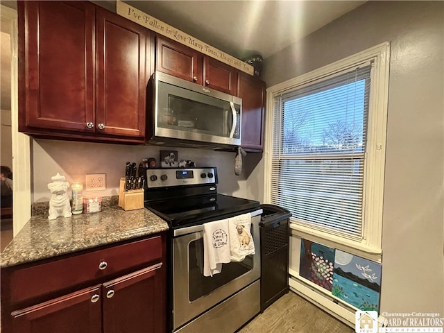 kitchen featuring dark stone countertops, baseboard heating, stainless steel appliances, and light hardwood / wood-style flooring