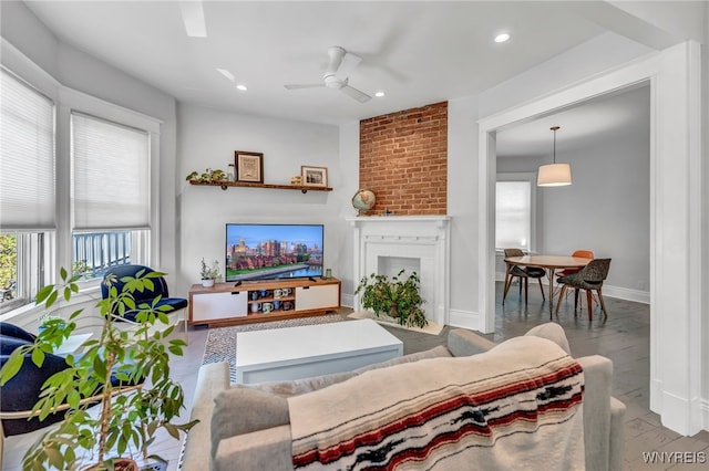 living room featuring ceiling fan, wood-type flooring, and a brick fireplace