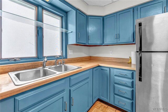 kitchen with blue cabinetry, light parquet flooring, stainless steel refrigerator, and sink