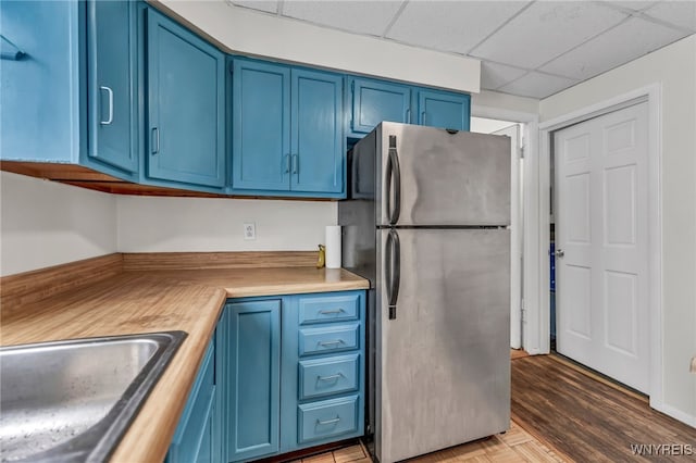 kitchen with wood counters, light wood-type flooring, blue cabinetry, and stainless steel refrigerator