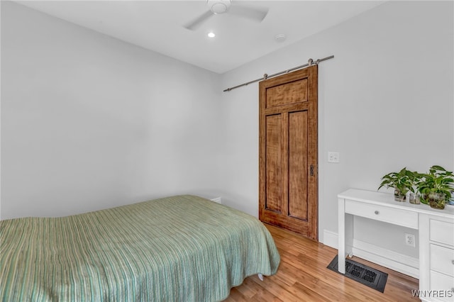 bedroom with a barn door, ceiling fan, and light hardwood / wood-style floors