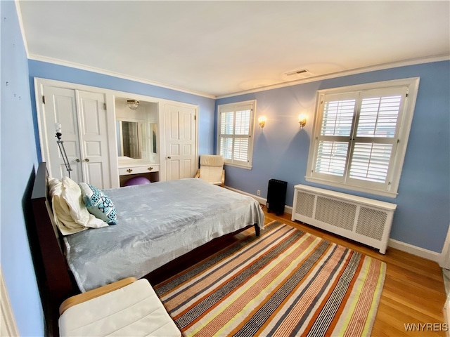 bedroom featuring hardwood / wood-style flooring, radiator heating unit, crown molding, and multiple windows