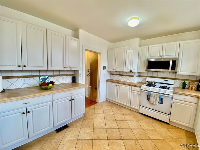 kitchen with backsplash, white gas range, white cabinets, and light tile patterned floors