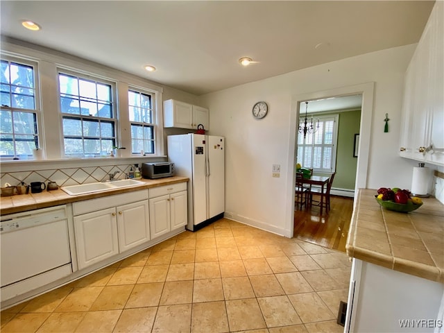 kitchen featuring plenty of natural light, white appliances, sink, white cabinetry, and tile counters